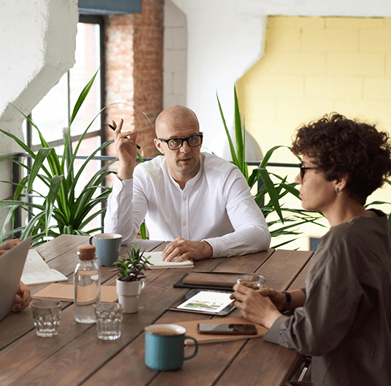 Two Century 21 agents sitting at a long table in a brightly lit room. The man has a notebook in front of him and the woman has a tablet.