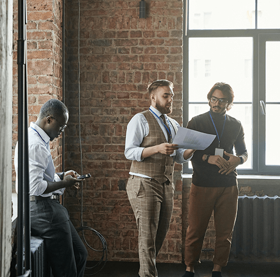 Three Century 21 agents standing and speaking near an office window while reviewing a piece of paper
